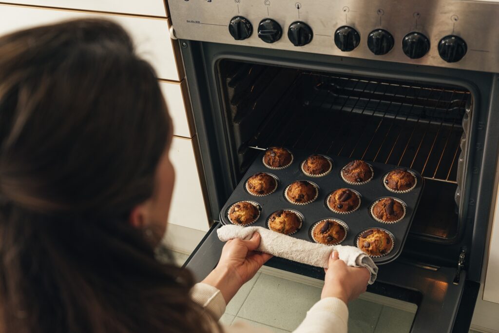 A woman taking out baked muffins from the oven